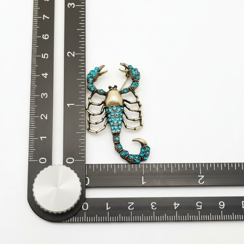 Scorpion-shaped brooch with turquoise stones on a white surface with a ruler for scale.