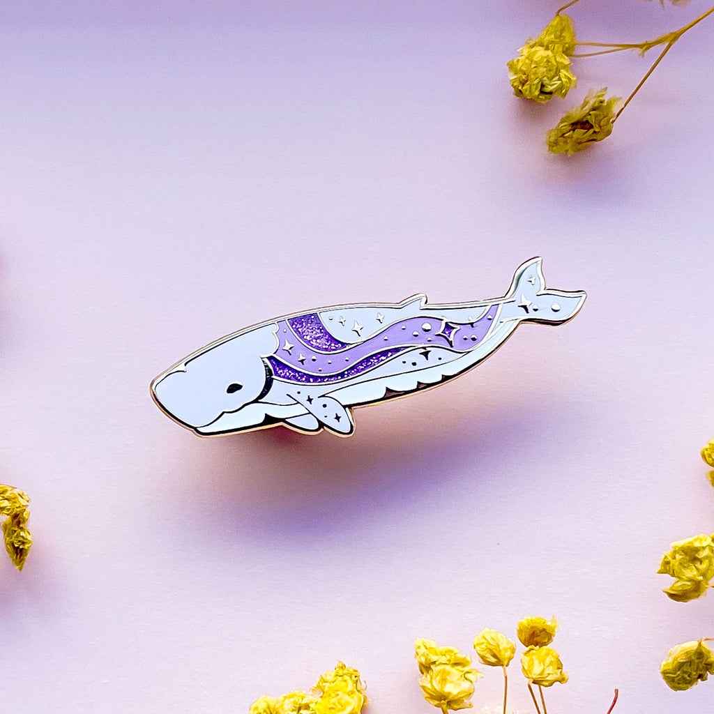 Decorative whale-shaped pin with purple design on a light purple background with yellow flowers.