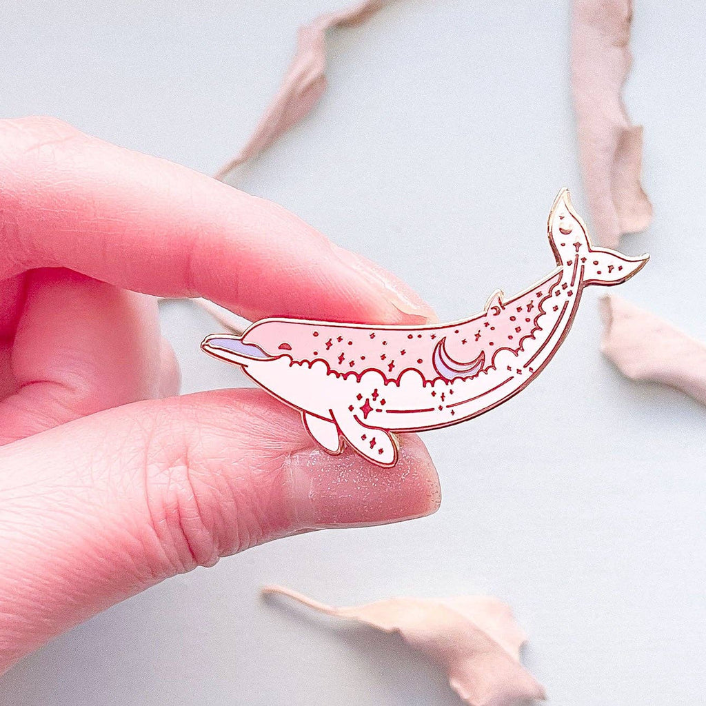 Hand holding a pink dolphin-shaped object with decorative elements on a light background