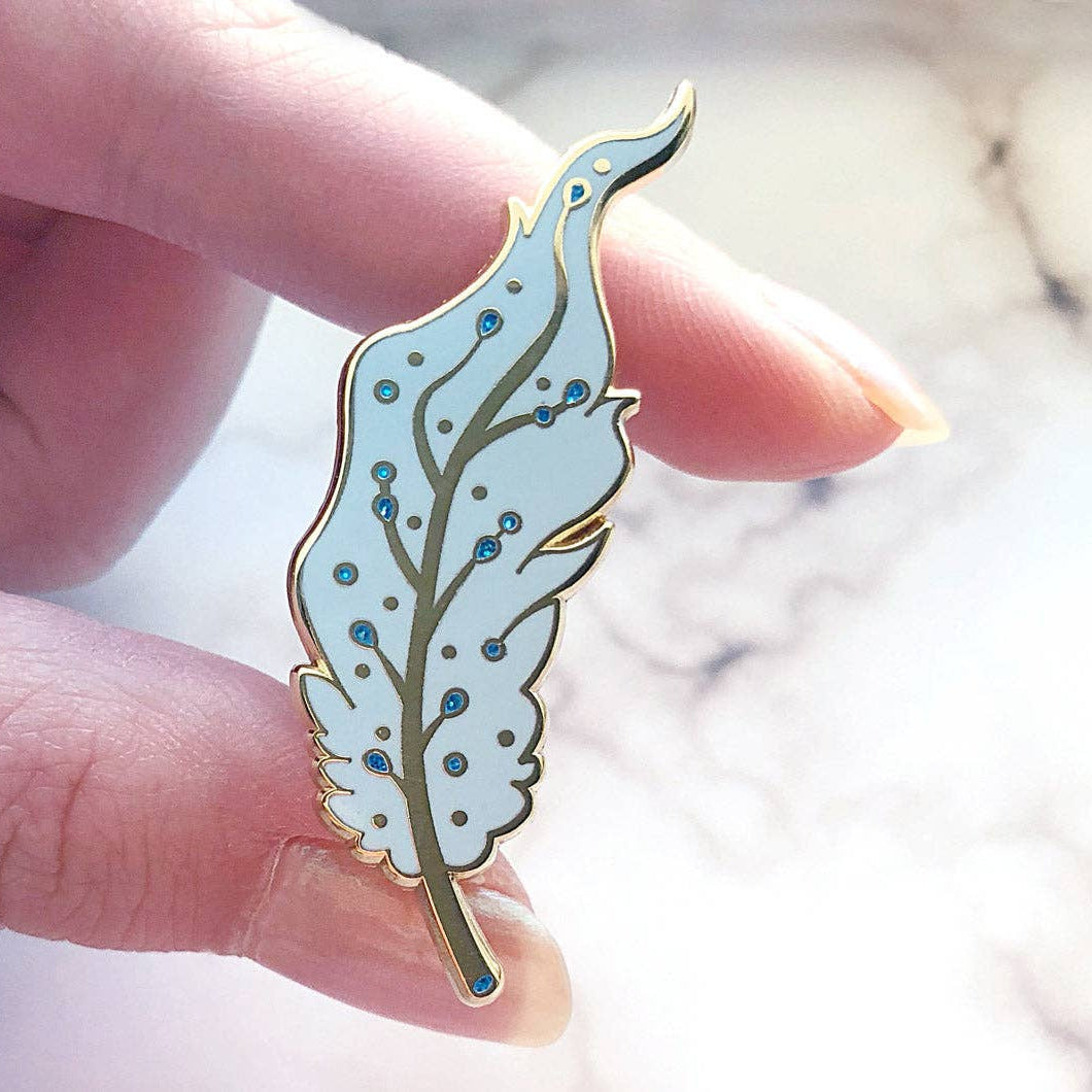 Hand holding a decorative Pegasus pin with a marble background