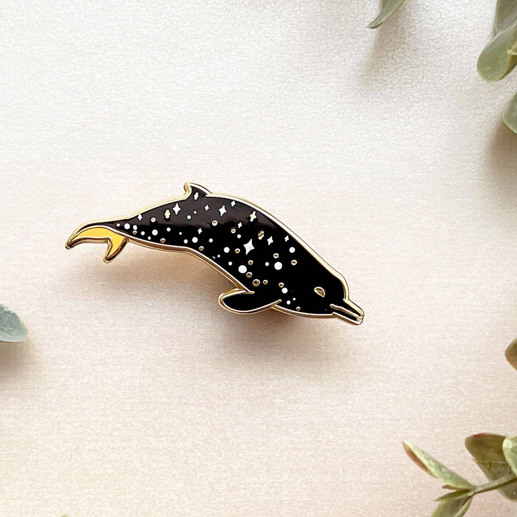 Dolphin-shaped pin on a light background with green leaves