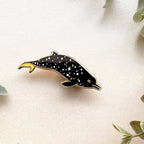 Dolphin-shaped pin on a light background with green leaves