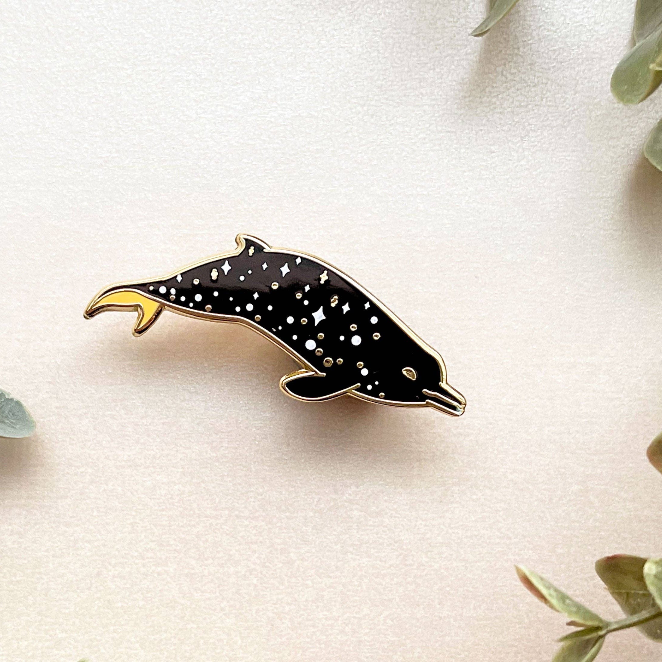 Dolphin-shaped pin on a light background with green leaves