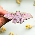Pink moth-shaped pin held by a hand with a light background