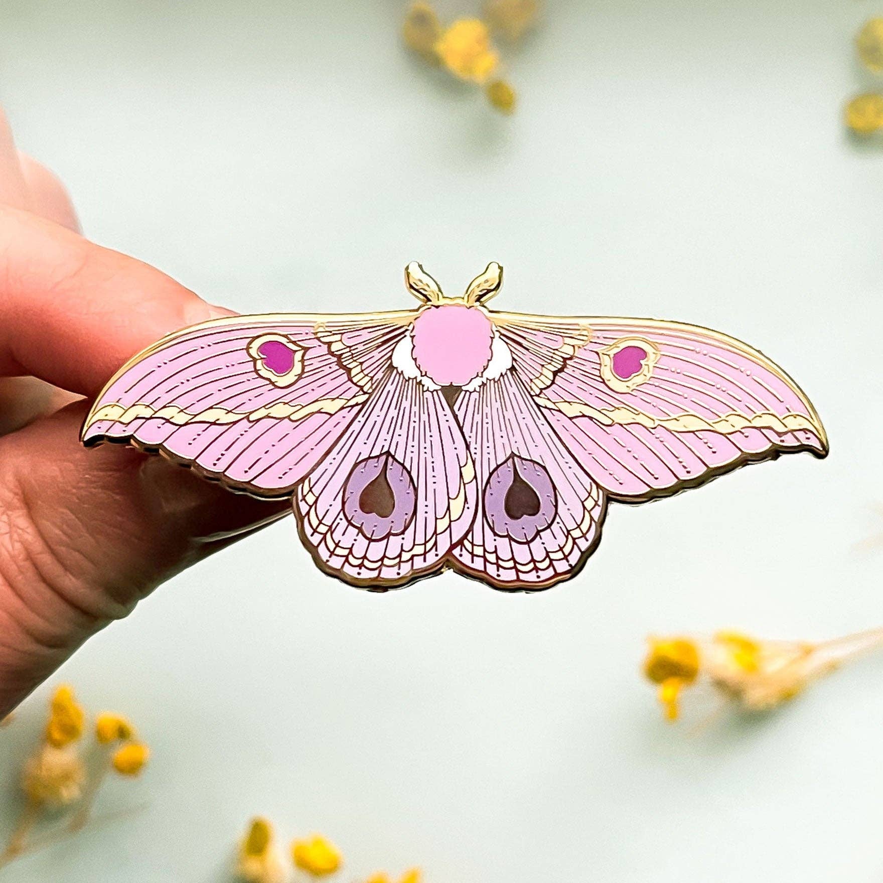 Pink moth-shaped pin held by a hand with a light background