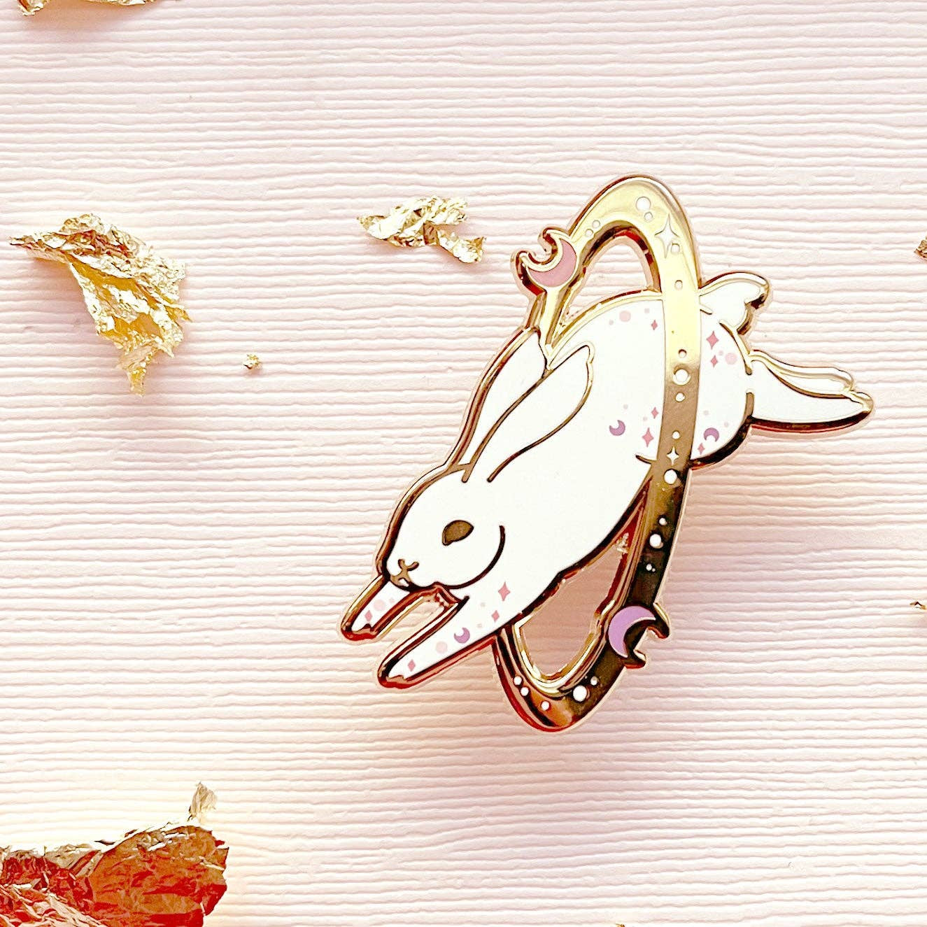Metallic bunny-shaped brooch on a textured surface with gold flakes