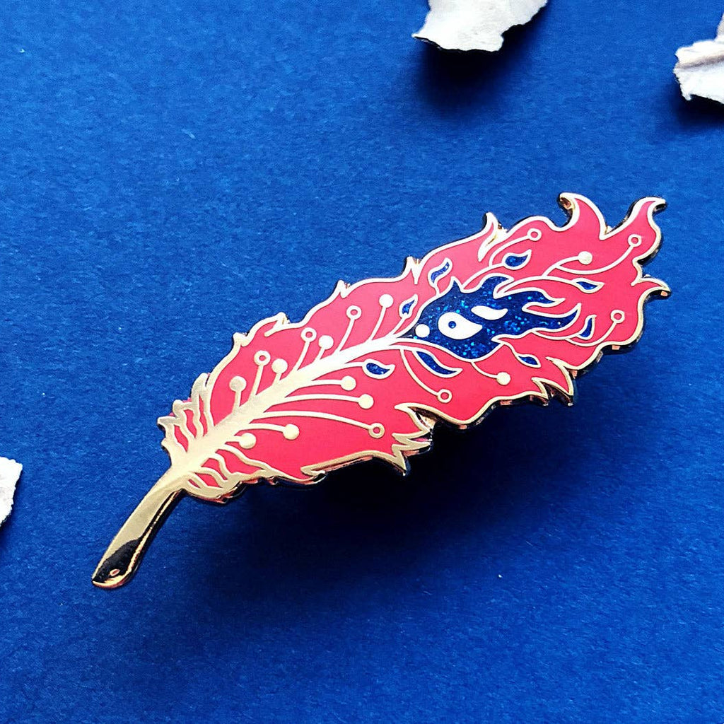 Feather-shaped pin with a blue eye design on a blue background