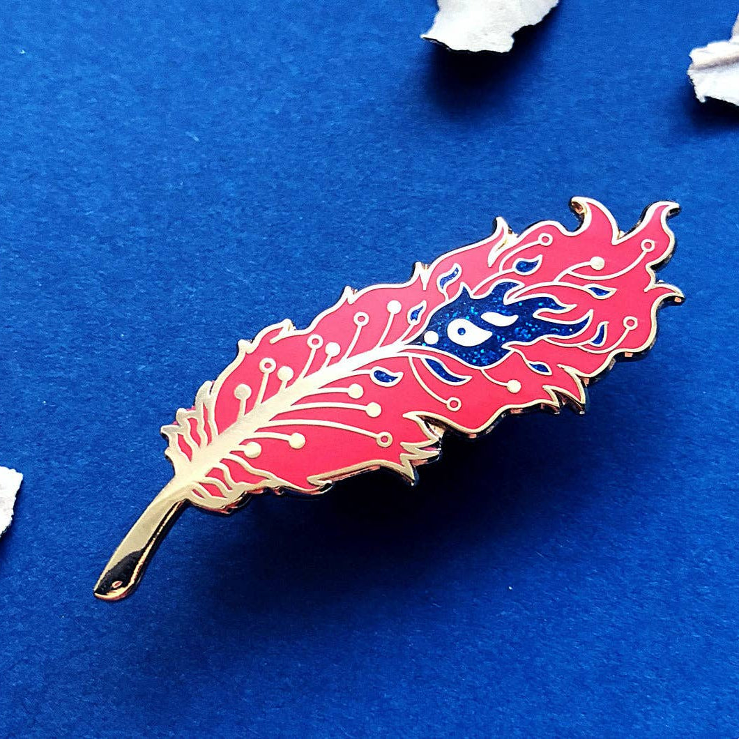 Feather-shaped pin with a blue eye design on a blue background