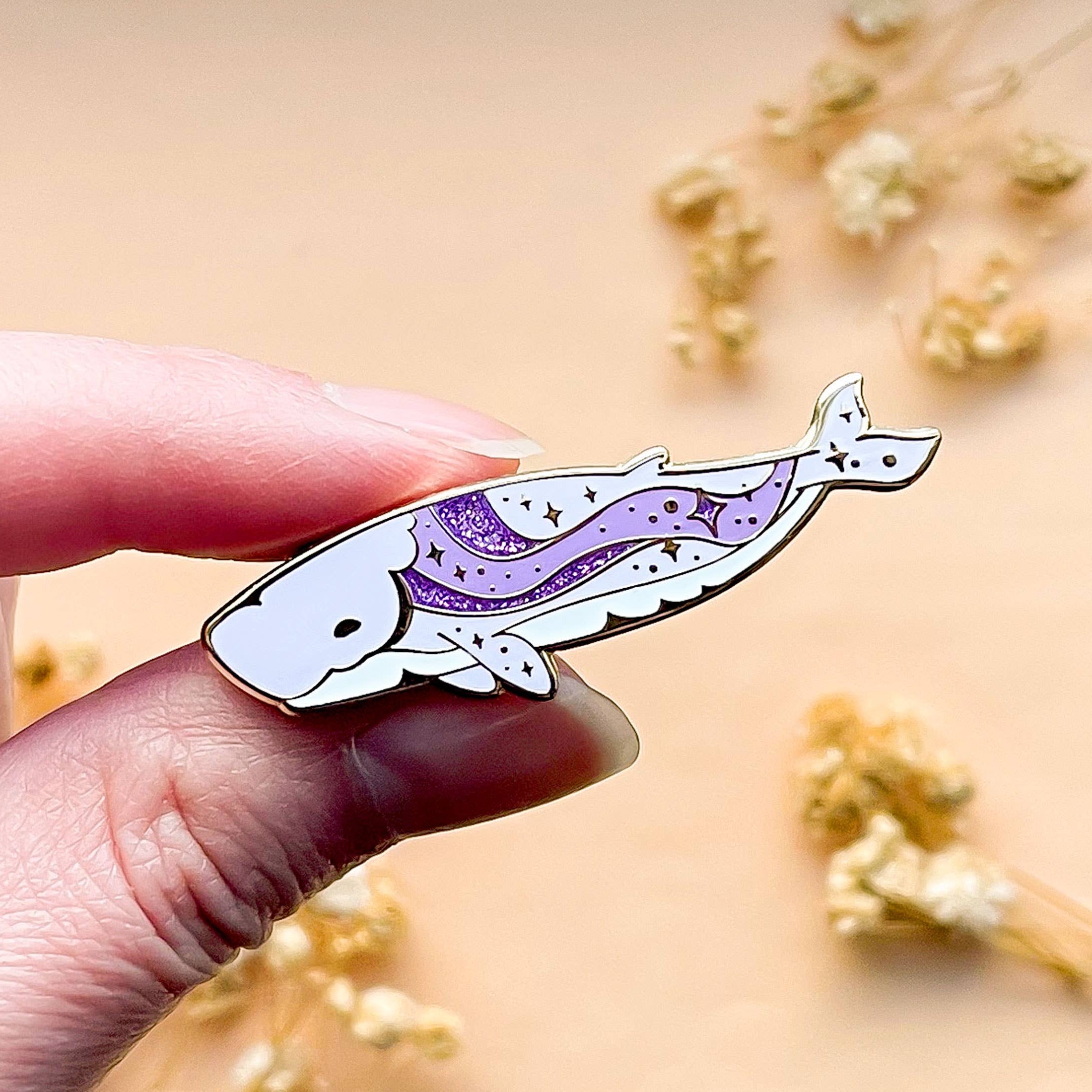 Hand holding a whale-shaped pin with a purple design against a blurred natural background