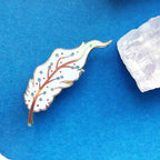 Decorative feather pin on a blue background with white stones
