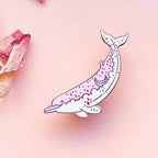 Decorative pin with a whale design on a pink background with floral elements