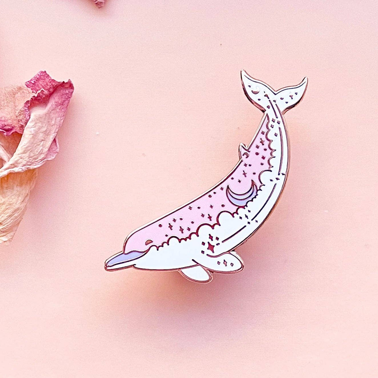 Decorative pin with a whale design on a pink background with floral elements