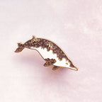 Detailed dolphin-shaped pin on a light pink background