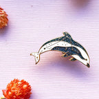 Dolphin-shaped brooch on a textured pink background with orange floral elements