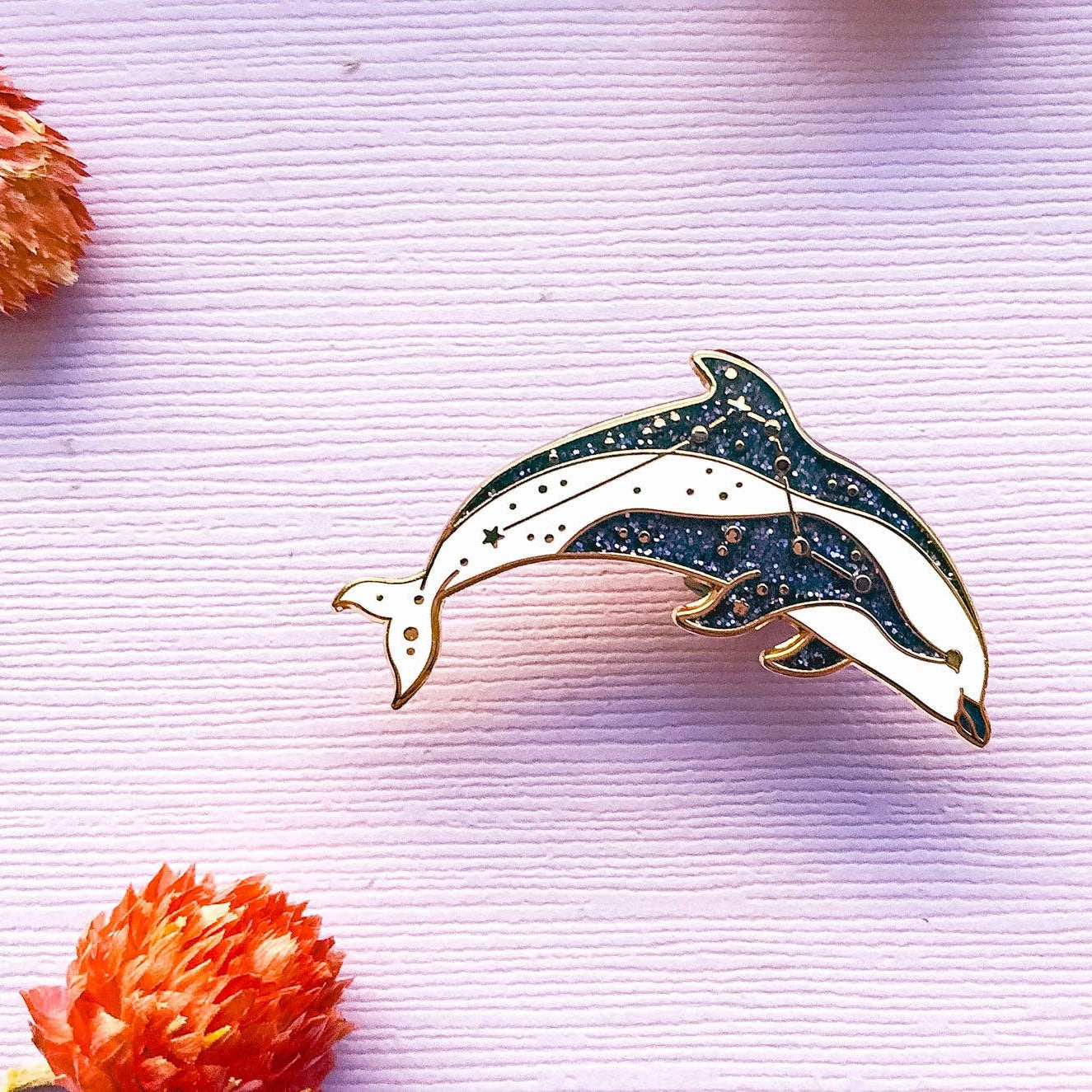 Dolphin-shaped brooch on a textured pink background with orange floral elements