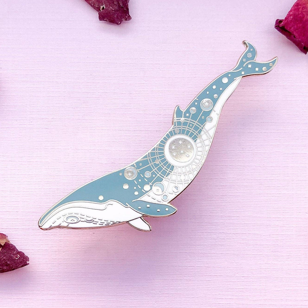 Decorative whale-shaped object on a pink surface with dried flowers.