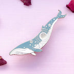 Decorative whale-shaped object on a pink surface with dried flowers.