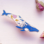 Colorful whale-shaped pin on a textured surface with dried flowers.