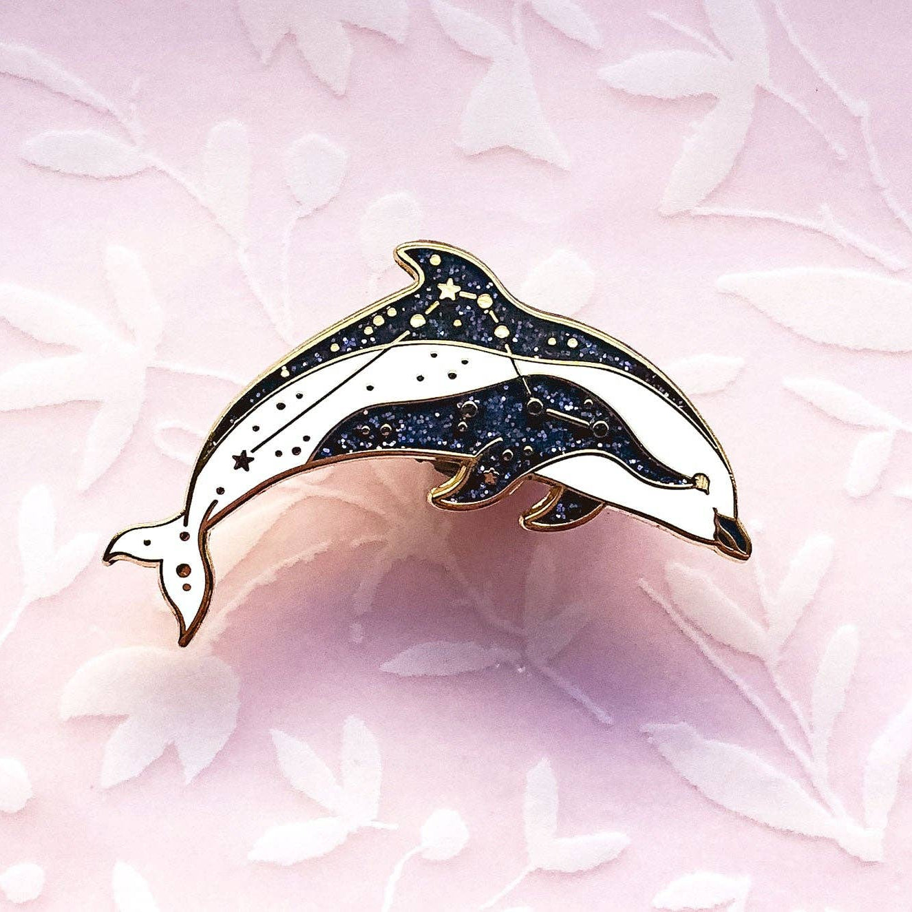 Dolphin-shaped brooch with black and gold details on a pink floral background