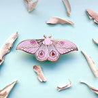 Pink butterfly-shaped lapel pin on a light blue background with beige butterfly wings scattered around