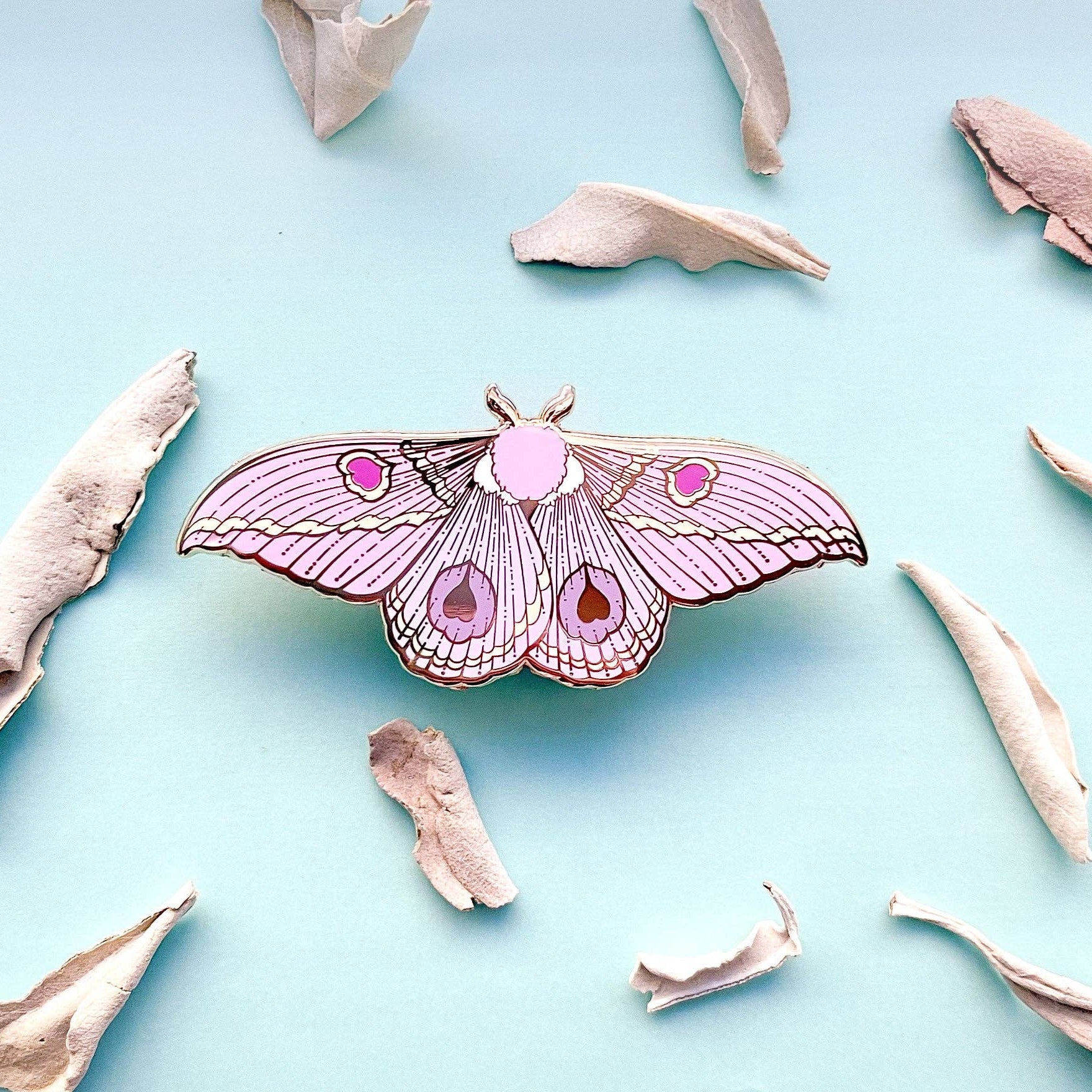 Pink butterfly-shaped lapel pin on a light blue background with beige butterfly wings scattered around