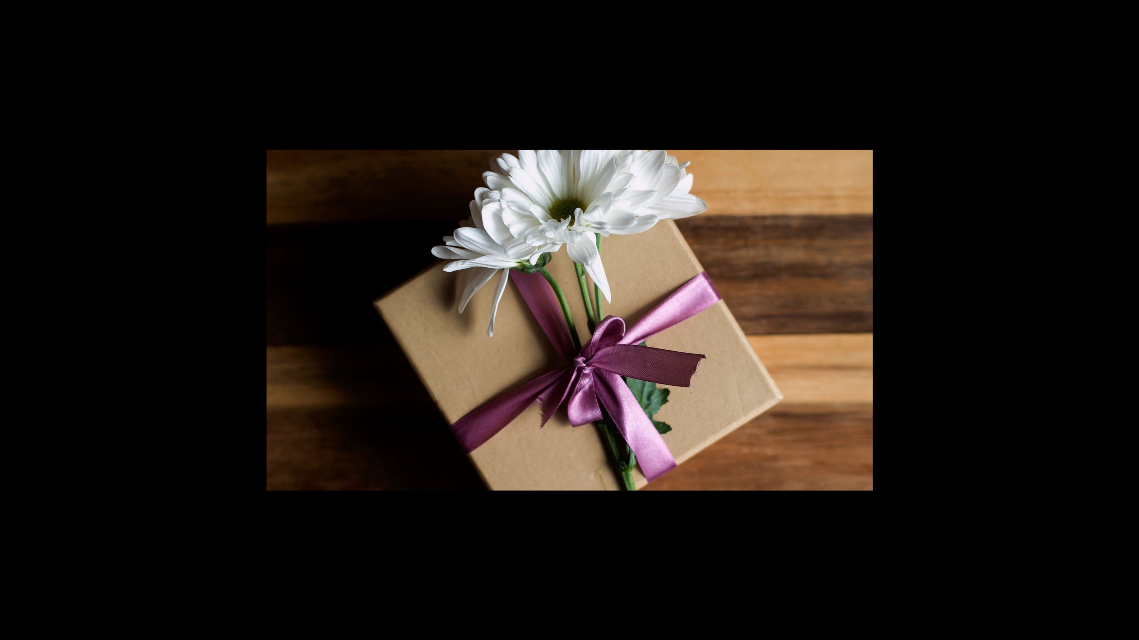 Gift box with a purple ribbon and white flowers on a wooden surface